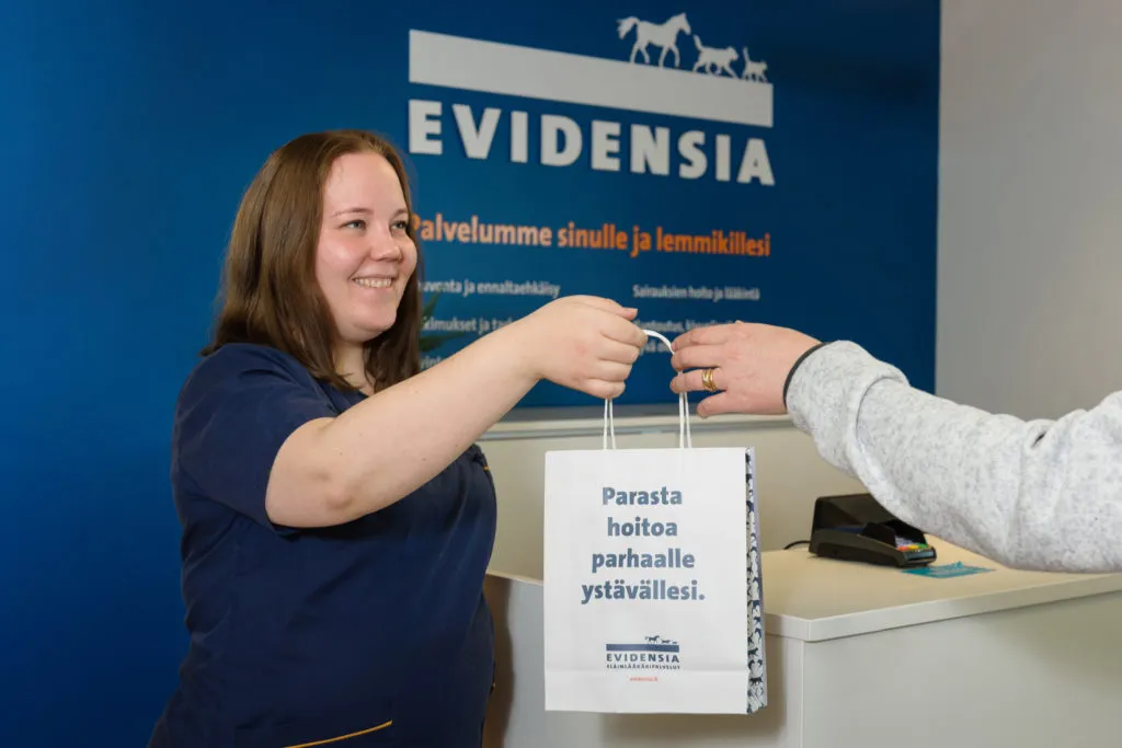 klinikkaeläinhoitaja ojentaa asiakkaalle paperipussissa tarvikkeita lemmikkiä varten